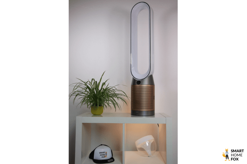 Очиститель воздуха и башенный вентилятор Purifier Cool Formaldehyd от Дайсон стоит на полке рядом с растением.